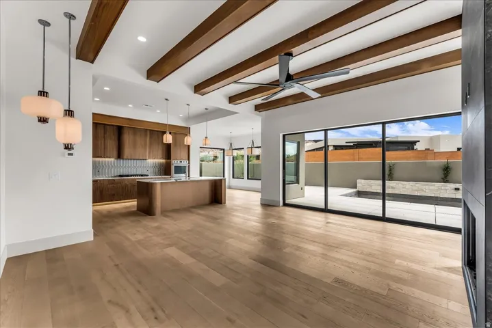 Expansive wood-finish flooring, exposed wood ceiling beams, a contemporary kitchen island, built-in stainless steel appliances, and large sliding glass doors leading to a private outdoor space