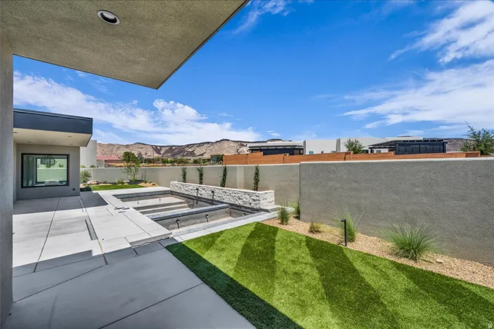 Spacious backyard featuring a multi-tiered water feature with stone accents, extensive concrete patio areas, and a combination of artificial turf and gravel landscaping