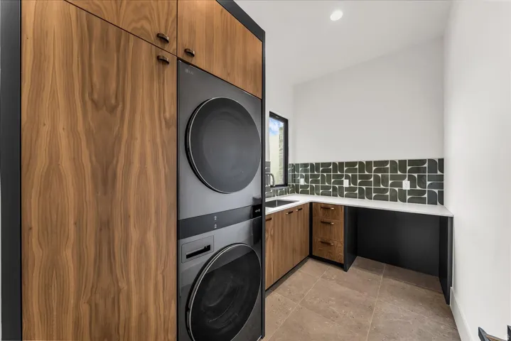 Integrated stacked washer and dryer, wood-finish cabinetry, tile backsplash, undermount sink, and durable tile flooring