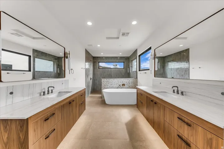 Dual wood-finish vanities with undermount sinks and extensive countertop space, freestanding soaking tub, and a large tile-surround shower