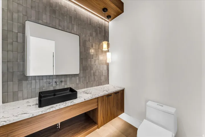 Wood-finish floating vanity with a stone countertop, vessel sink, and wall-mounted faucet