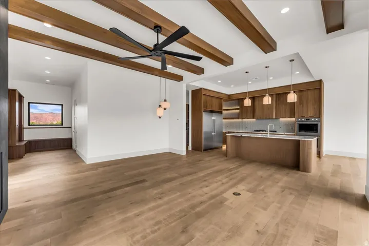 Hardwood-finish flooring, exposed ceiling beams, modern kitchen with built-in appliances, kitchen island with integrated sink, and recessed lighting