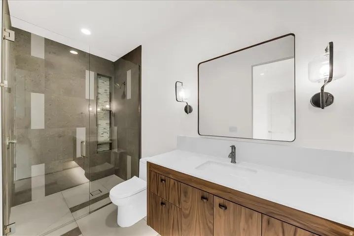 Glass-enclosed shower with a built-in bench, a wood-finish vanity with a single basin sink, a large rectangular mirror, and dual wall-mounted sconces