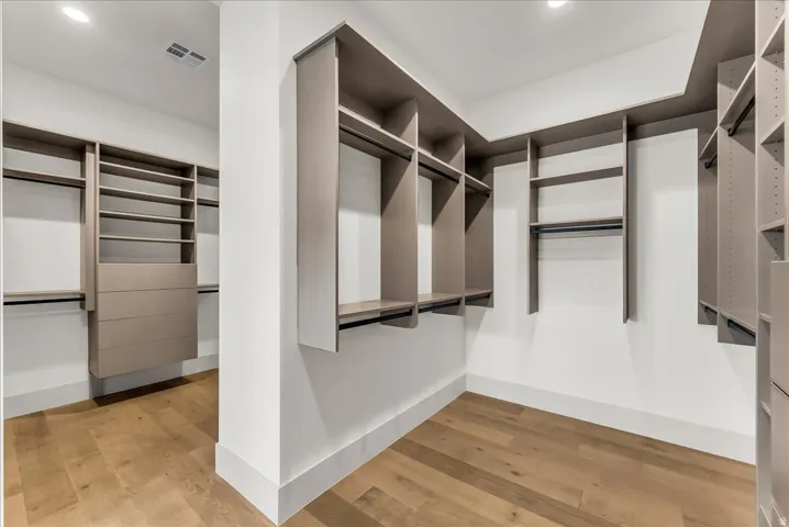 Walk-in closet featuring extensive built-in shelving, integrated drawers, multiple hanging rods, and wood-finish flooring