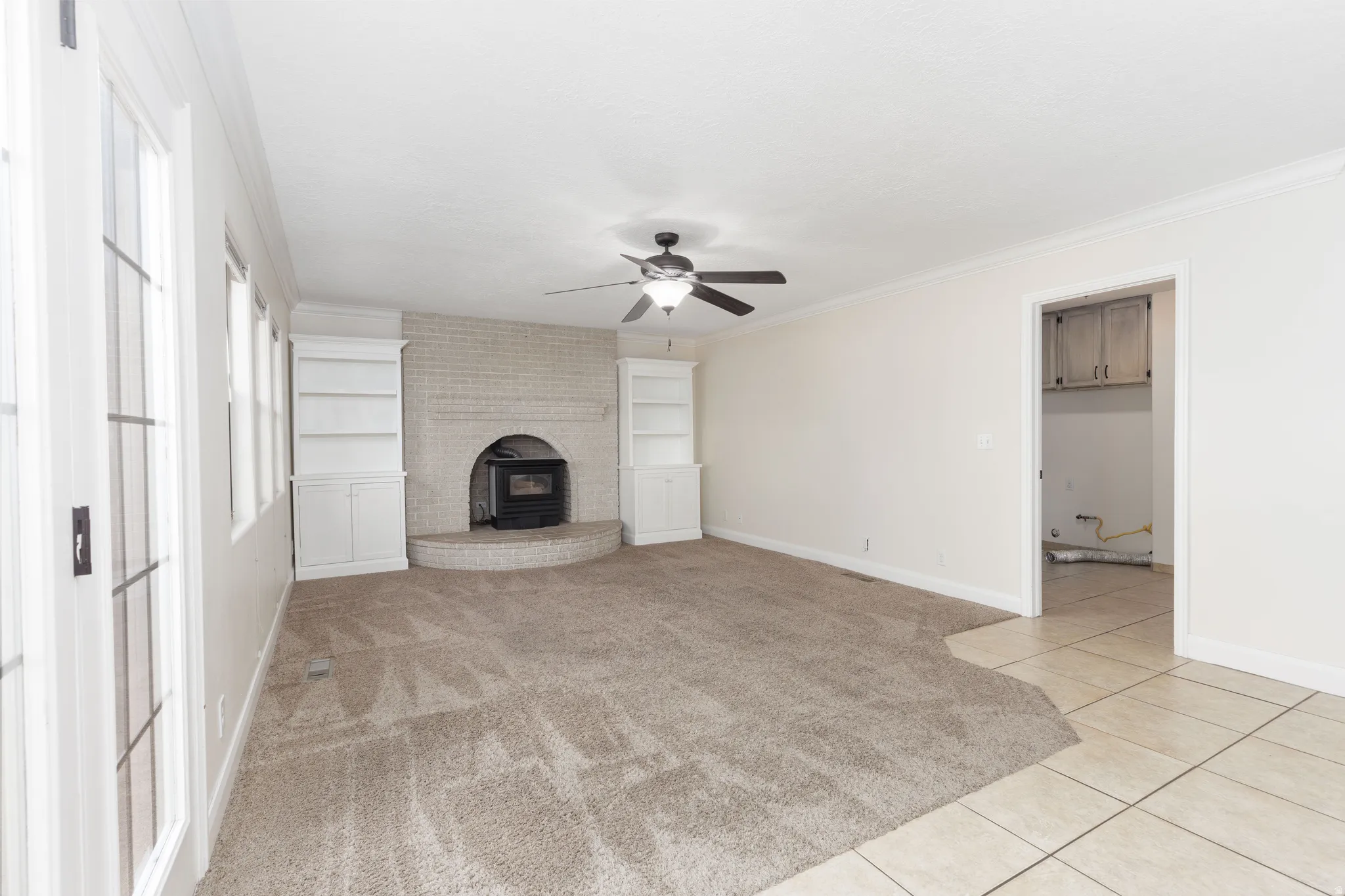 Carpeted living area with a white brick fireplace, wood stove, built-in shelving, and a ceiling fan
