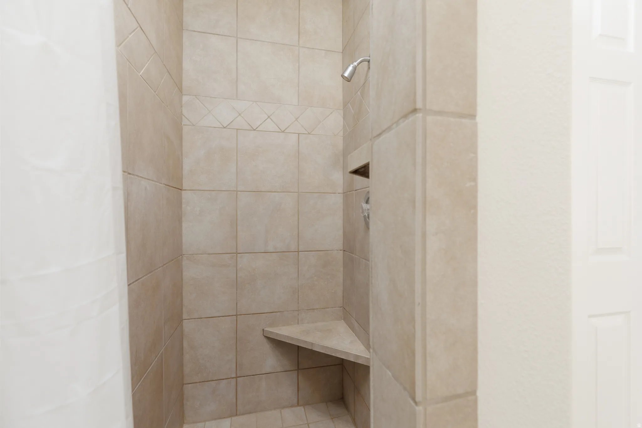 Tile-surround shower with a built-in corner bench, recessed niche, and a decorative tile band accent