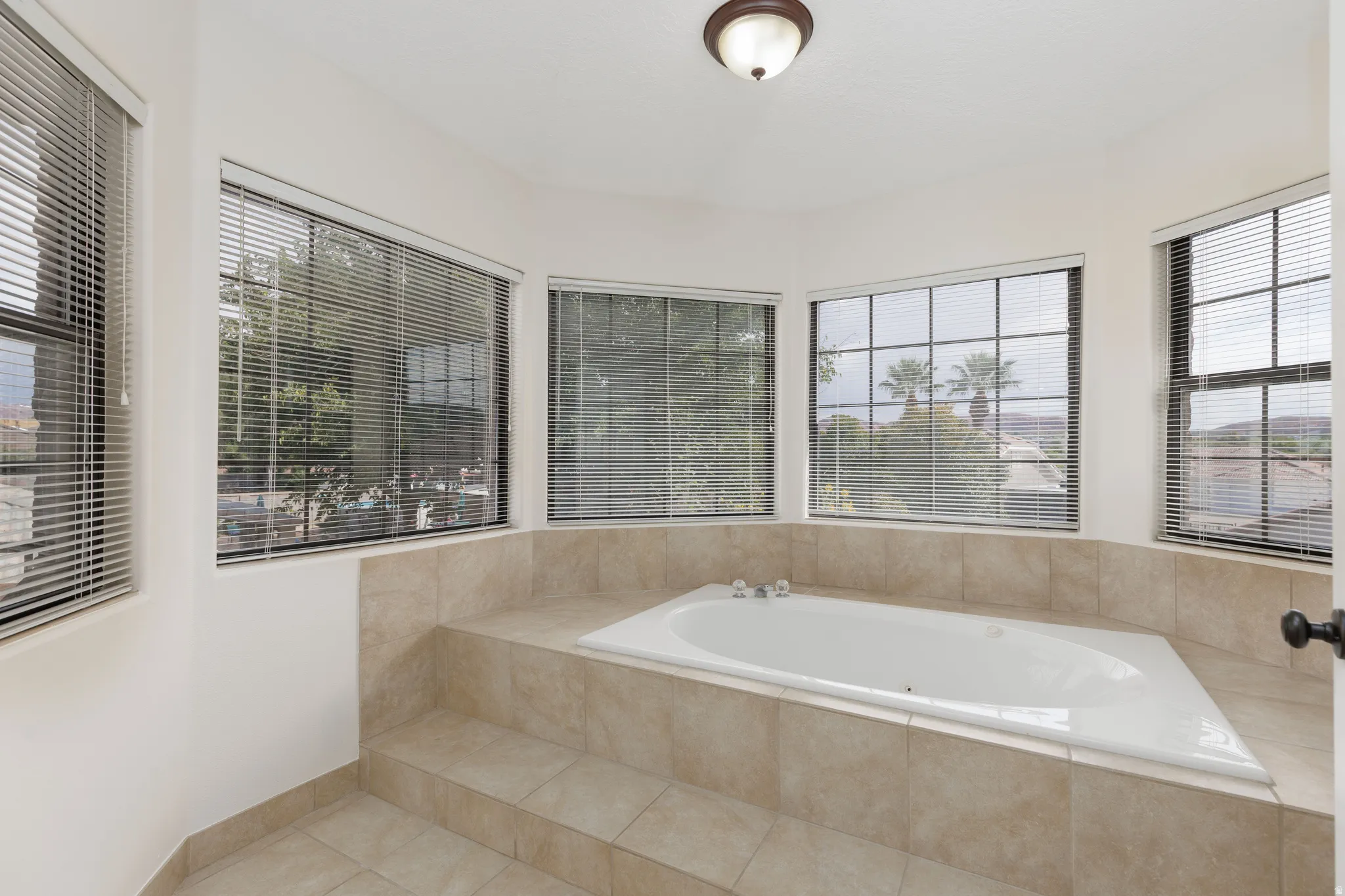 Built-in soaking tub with tile surround, bay window configuration, and recessed ceiling light fixture