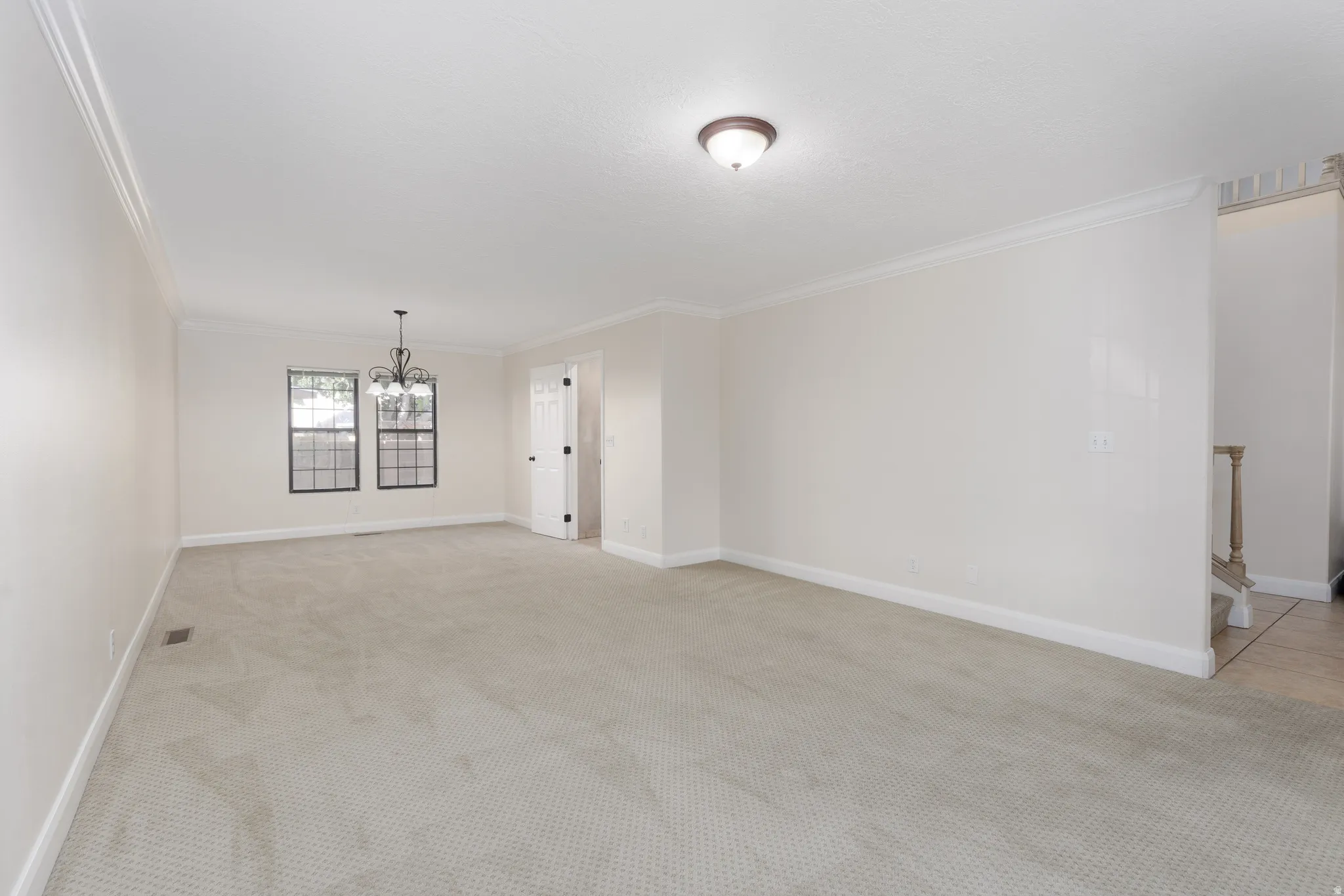 Carpeted flooring, crown molding, two gridded windows, a decorative chandelier, and a semi-flush ceiling light fixture