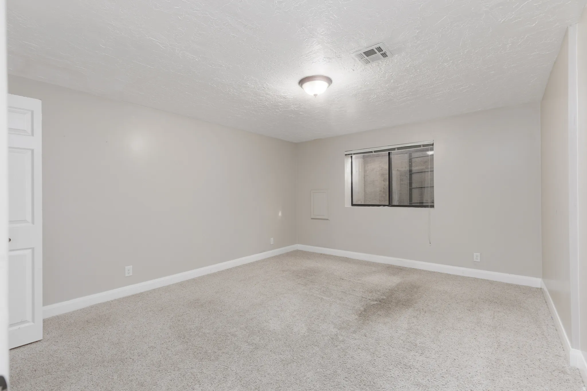 Neutral wall paint, carpet flooring, a window with blinds, and a flush-mount ceiling light fixture