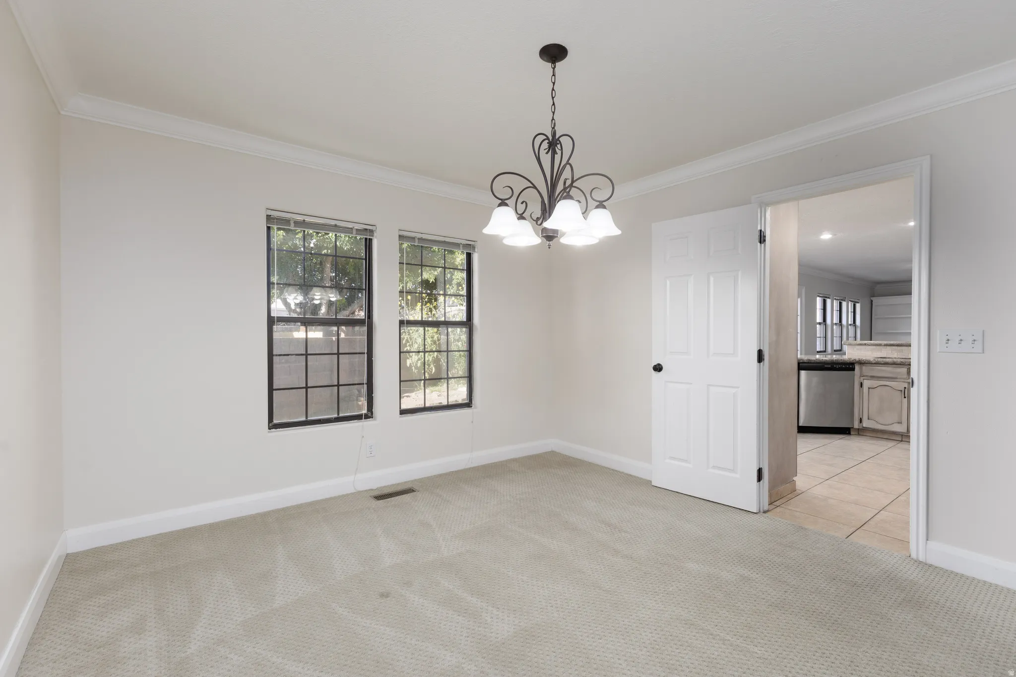 Carpeted room with crown molding, two windows, and a hanging chandelier