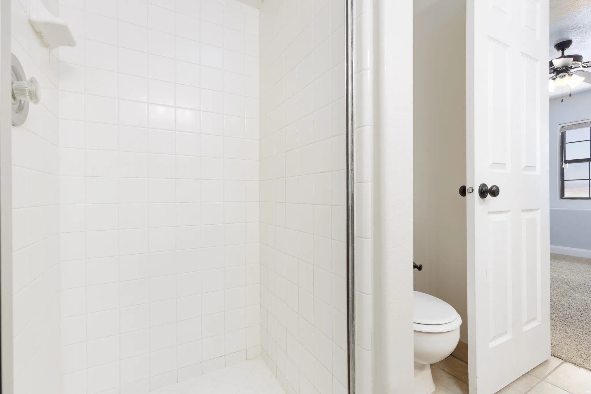 White tiled shower with chrome fixtures and glass enclosure