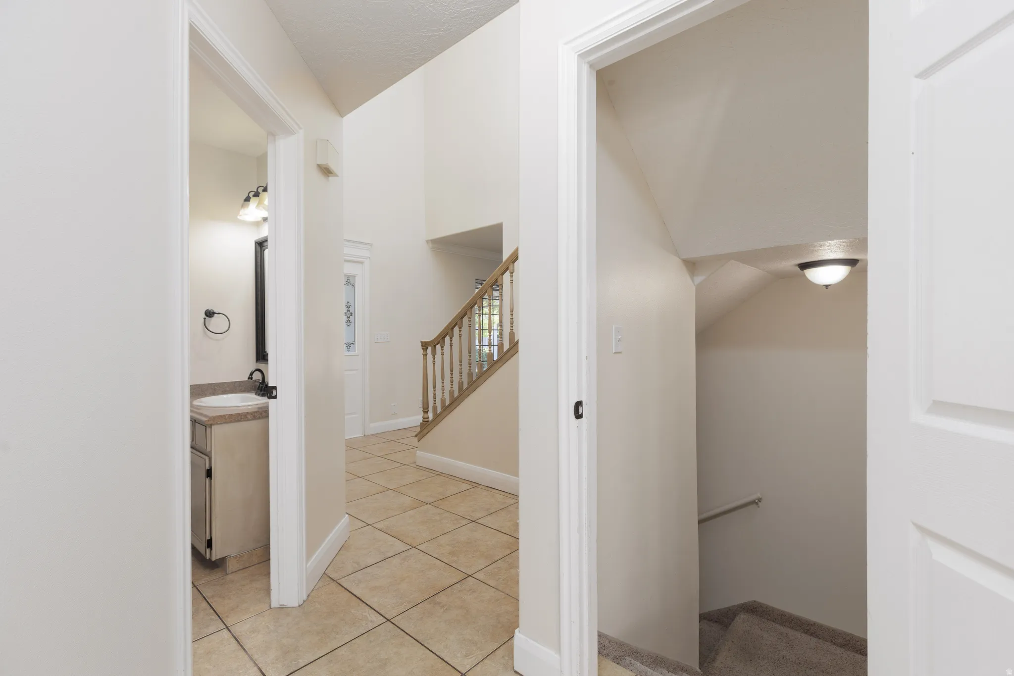Two-story foyer with tile flooring, wood staircase, and an attached vanity with a single basin sink