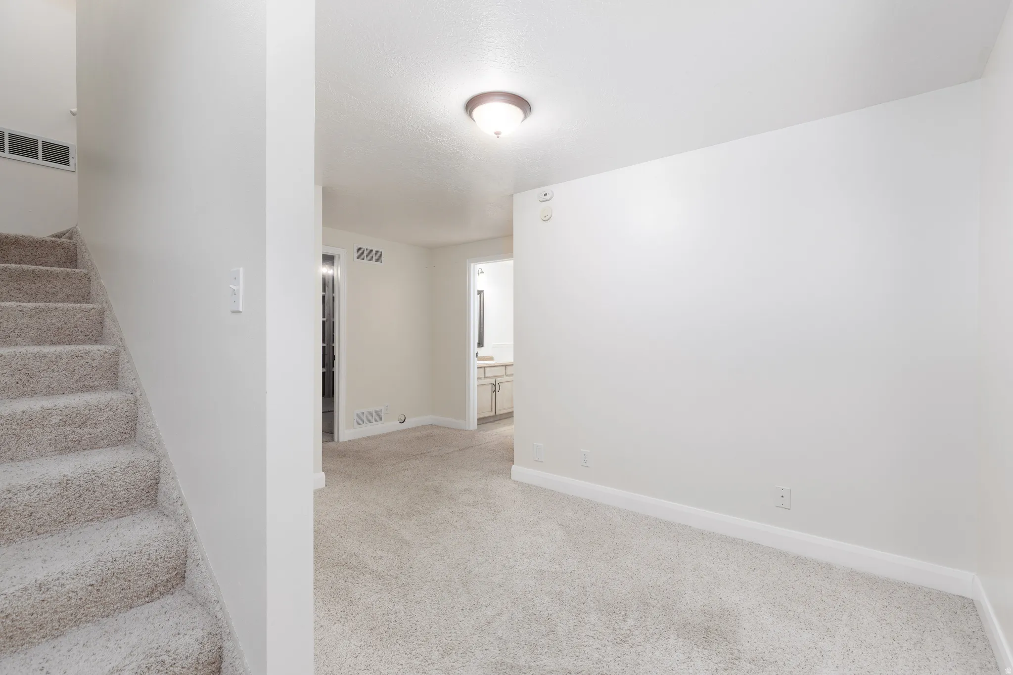 Carpeted staircase with white risers, light-colored wall-to-wall carpeting, and a flush mount ceiling light fixture