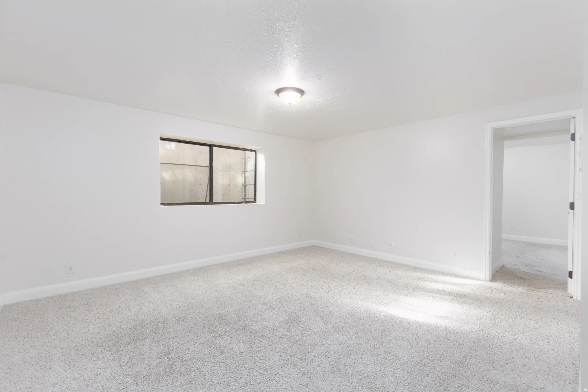 Recessed window with security bars, light gray carpet flooring, white painted walls, and a ceiling-mounted light fixture