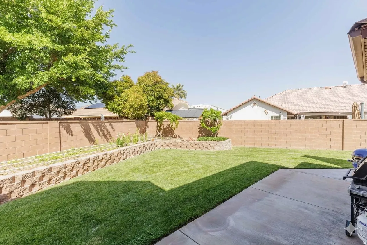 Expansive backyard featuring a manicured lawn, concrete patio, and tiered retaining wall with integrated planting beds