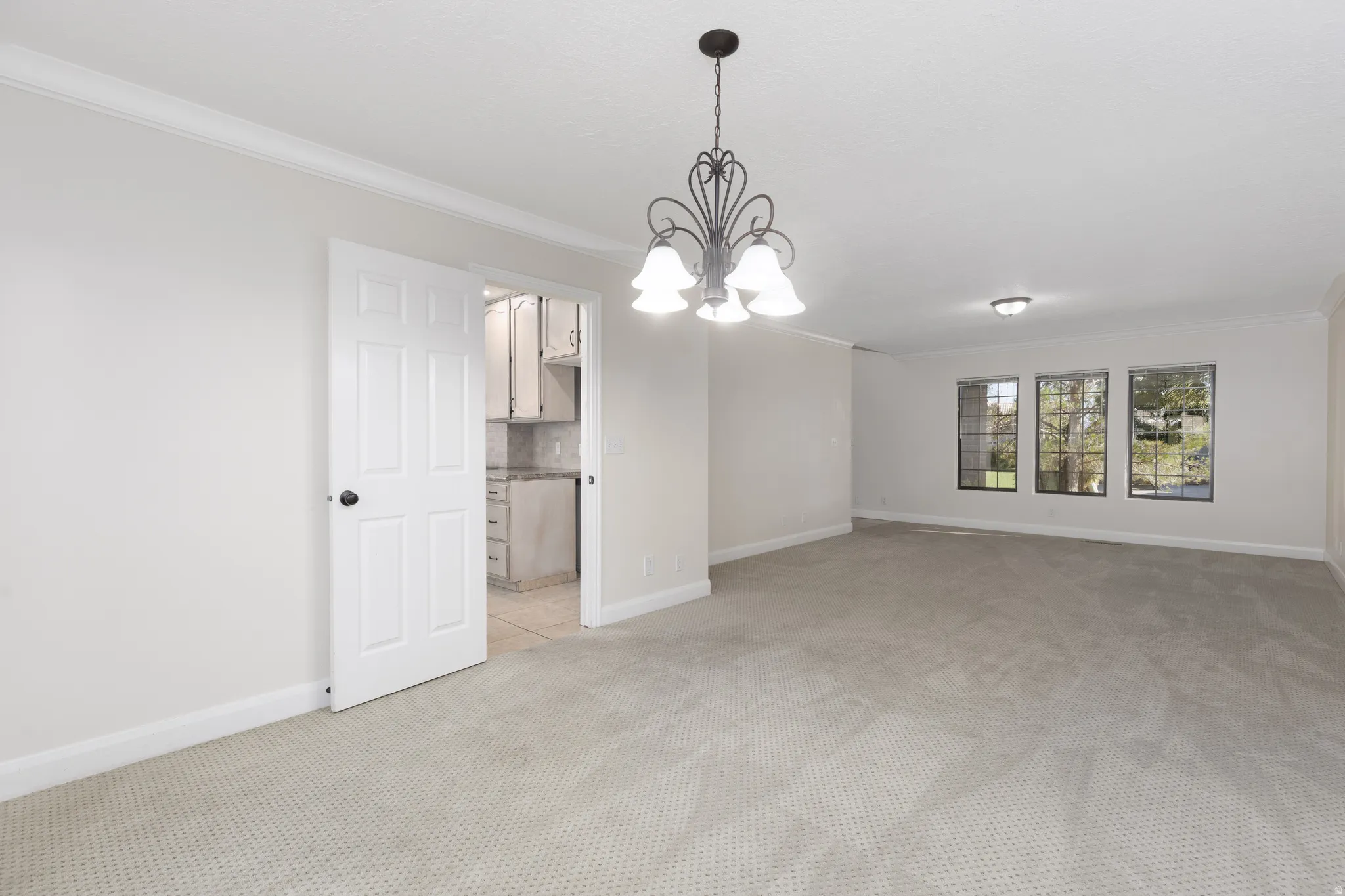 Spacious room featuring carpet flooring, crown molding, a decorative chandelier, and multiple windows