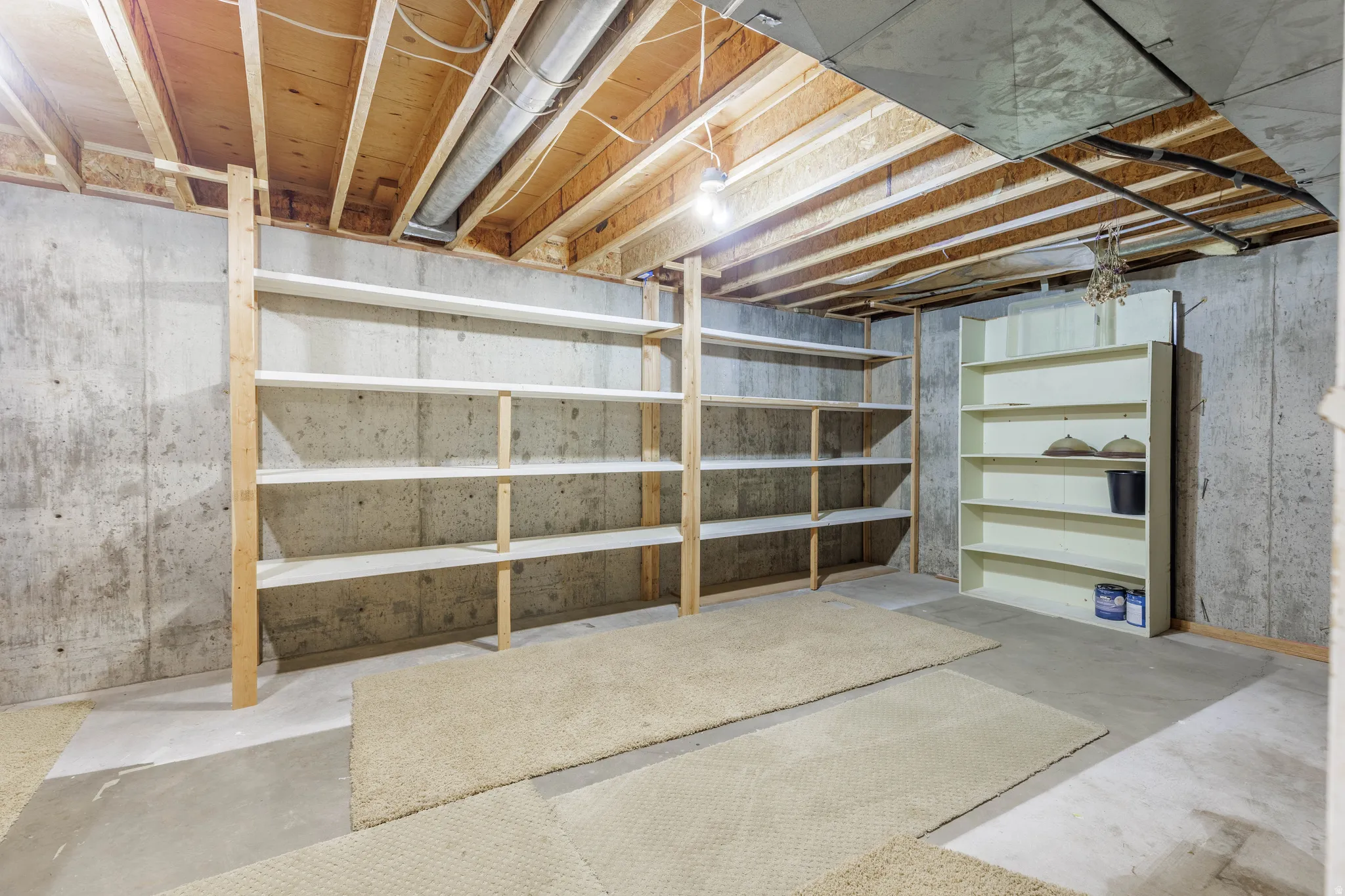 Exposed ceiling joists with visible ductwork, concrete walls, concrete flooring, built-in shelving, and additional shelving unit