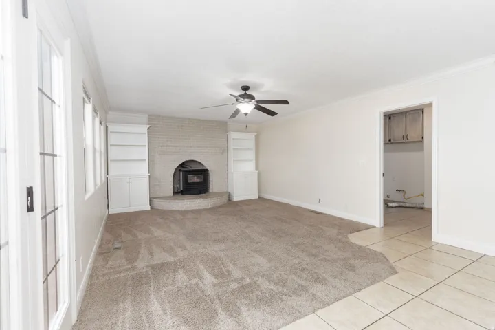 Carpeted living area with a white brick fireplace, wood stove, built-in shelving, and a ceiling fan