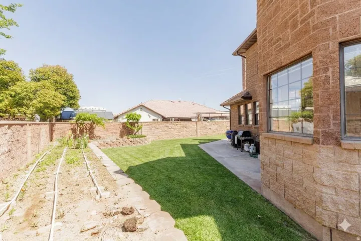 Stone exterior with multiple windows, concrete patio space, and a manicured lawn