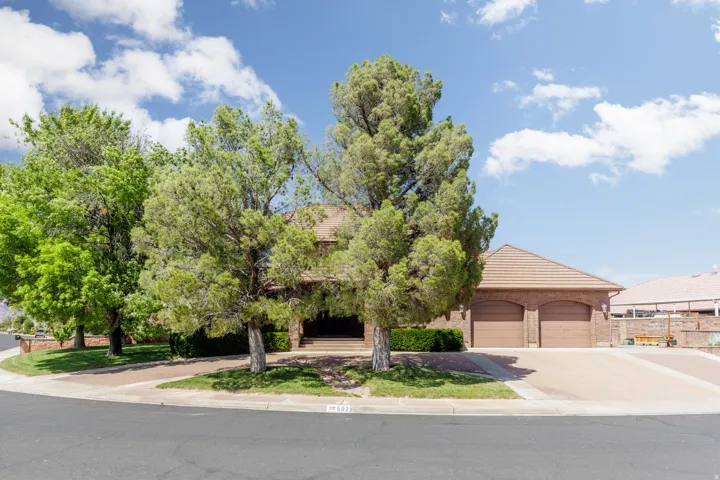 Brick exterior with a tiled roof, mature trees, and a two-car garage