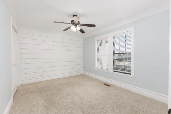 Wall-to-wall carpeting, white shiplap accent wall, white trim work, ceiling fan with integrated lighting, and dual windows