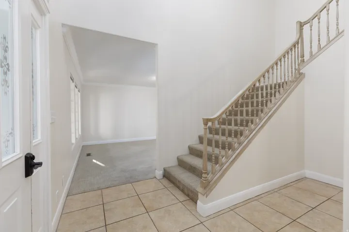 Foyer featuring tile flooring, a carpeted staircase with wood-finish balusters, and crown molding