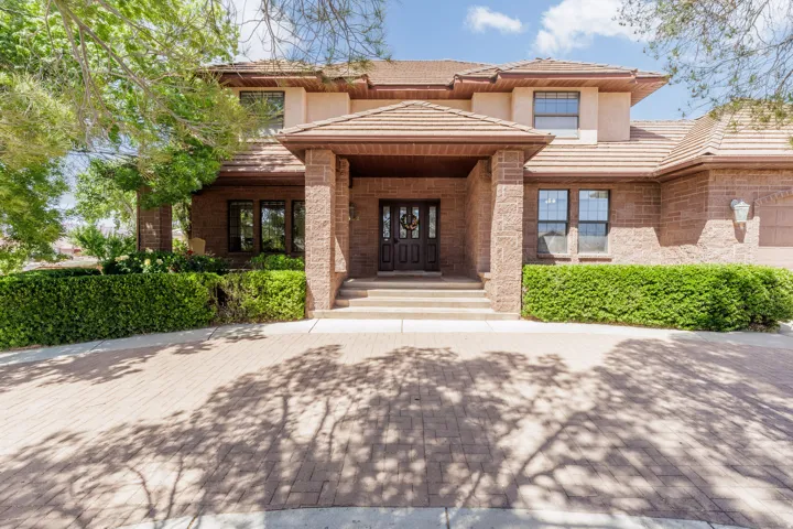 Brick exterior with a tiled roof, paver driveway, mature landscaping, prominent front entry with double doors, and an attached garage