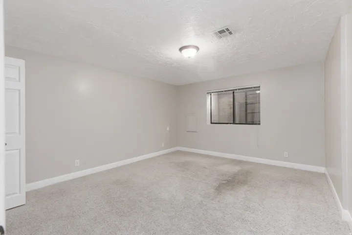 Neutral wall paint, carpet flooring, a window with blinds, and a flush-mount ceiling light fixture