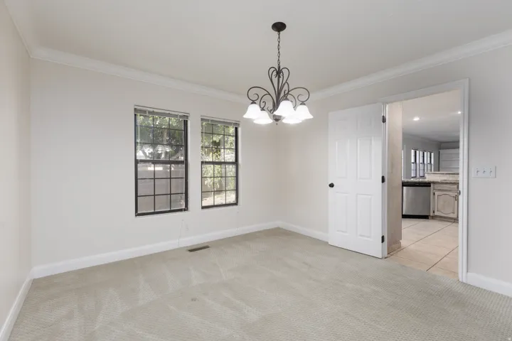 Carpeted room with crown molding, two windows, and a hanging chandelier