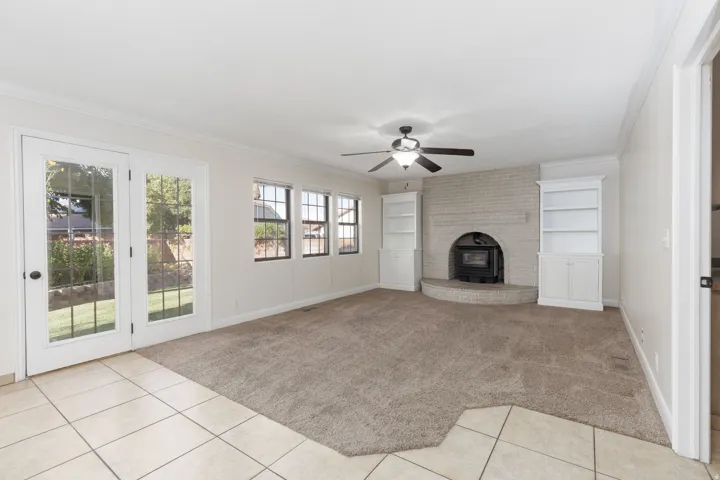 Living area with a corner brick fireplace, built-in shelving, and a ceiling fan