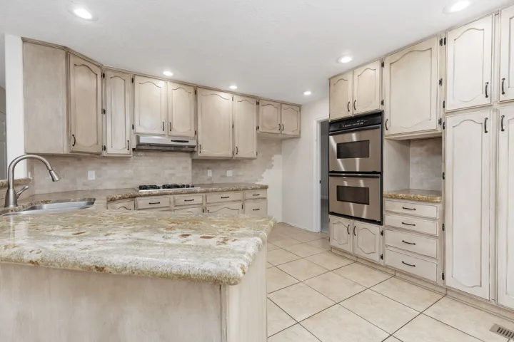 Kitchen featuring abundant cabinetry, granite countertops, tile backsplash, built-in double ovens, and tile flooring
