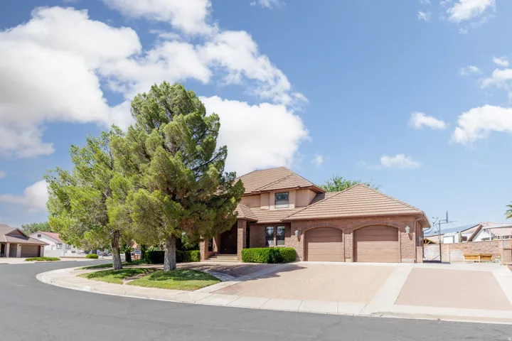 Brick exterior with a tile roof, featuring a two-car garage, mature trees, and a paver driveway