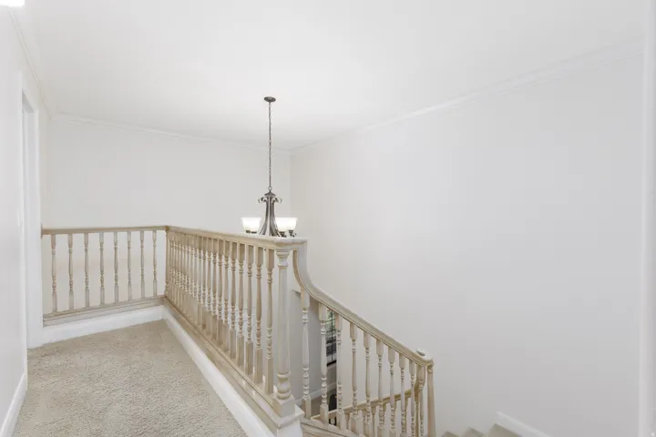 Stairway with carpeted treads and risers, featuring a light wood-finish balustrade and newel post