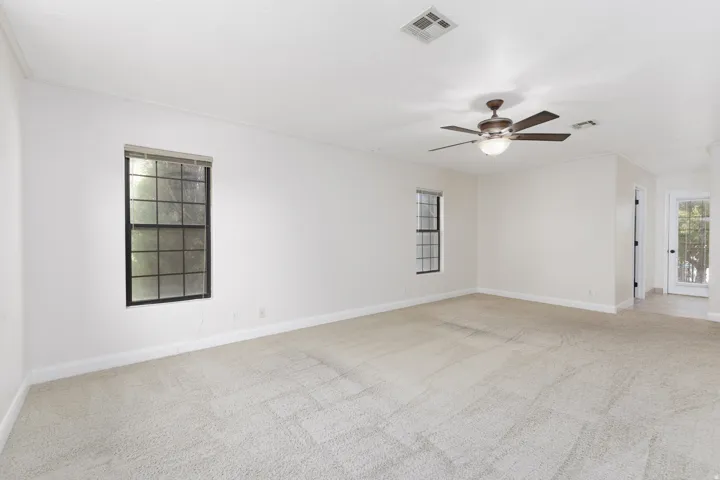 Spacious room featuring neutral carpeting, white walls, two single-hung windows, and a ceiling fan with integrated lighting