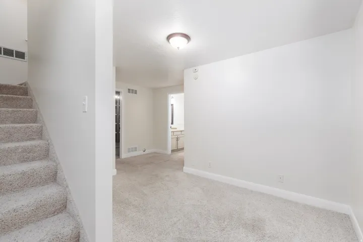 Carpeted staircase with white risers, light-colored wall-to-wall carpeting, and a flush mount ceiling light fixture