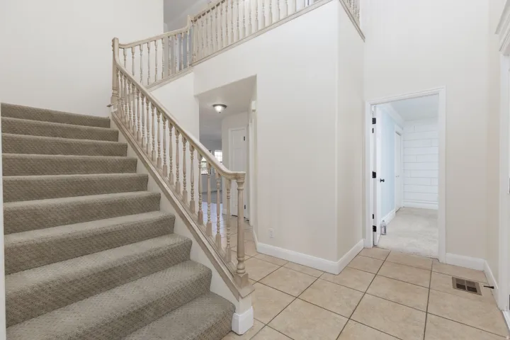 Two-story foyer featuring a carpeted staircase with wood banister, second-story landing, and tile flooring