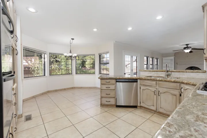 Kitchen with tile flooring, light-toned cabinetry, granite-finish countertops, stainless steel appliances, and a dining nook with bay windows