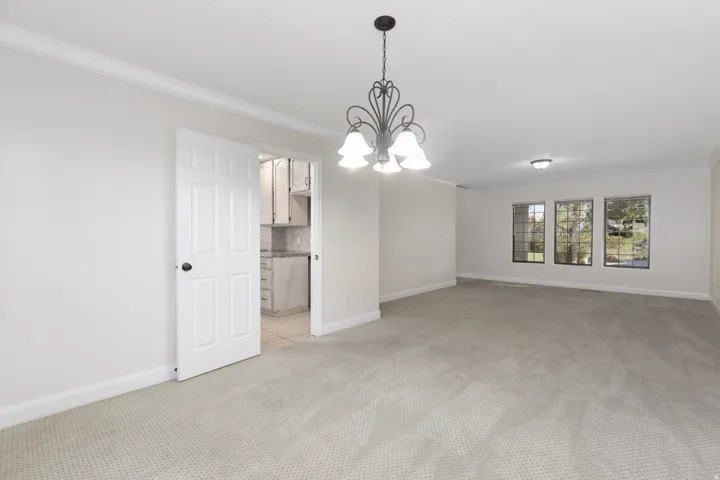 Spacious room featuring carpet flooring, crown molding, a decorative chandelier, and multiple windows