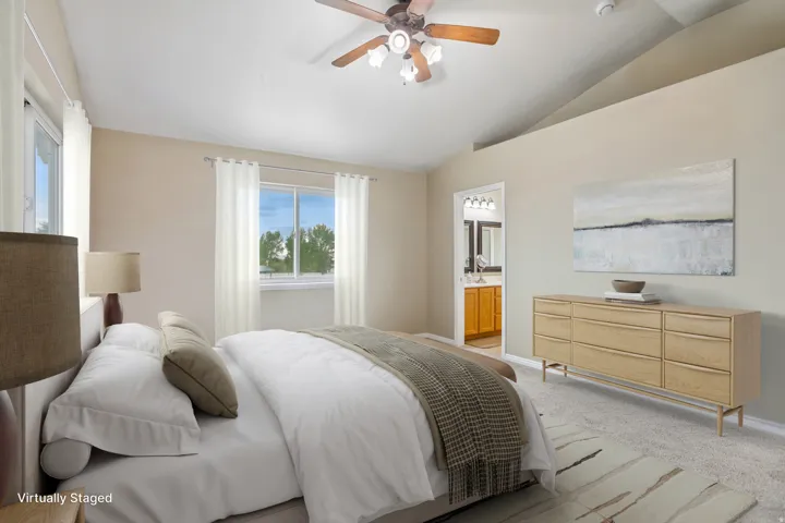 Primary bedroom virtually staged. Vaulted ceiling with a ceiling fan, dual windows, and carpeted flooring