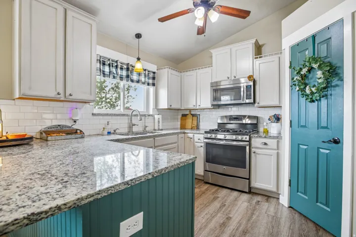 Kitchen with stainless steel appliances, light stone countertops, white cabinets, and lofted ceiling