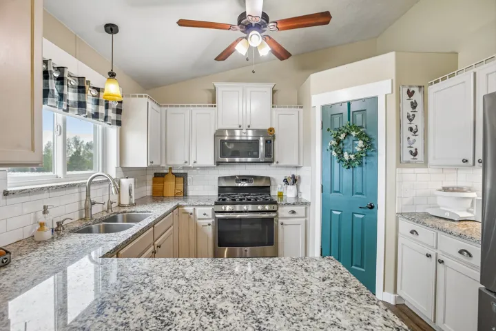 Kitchen featuring stainless steel appliances, light stone countertops, decorative backsplash, a ceiling fan, and lofted ceiling