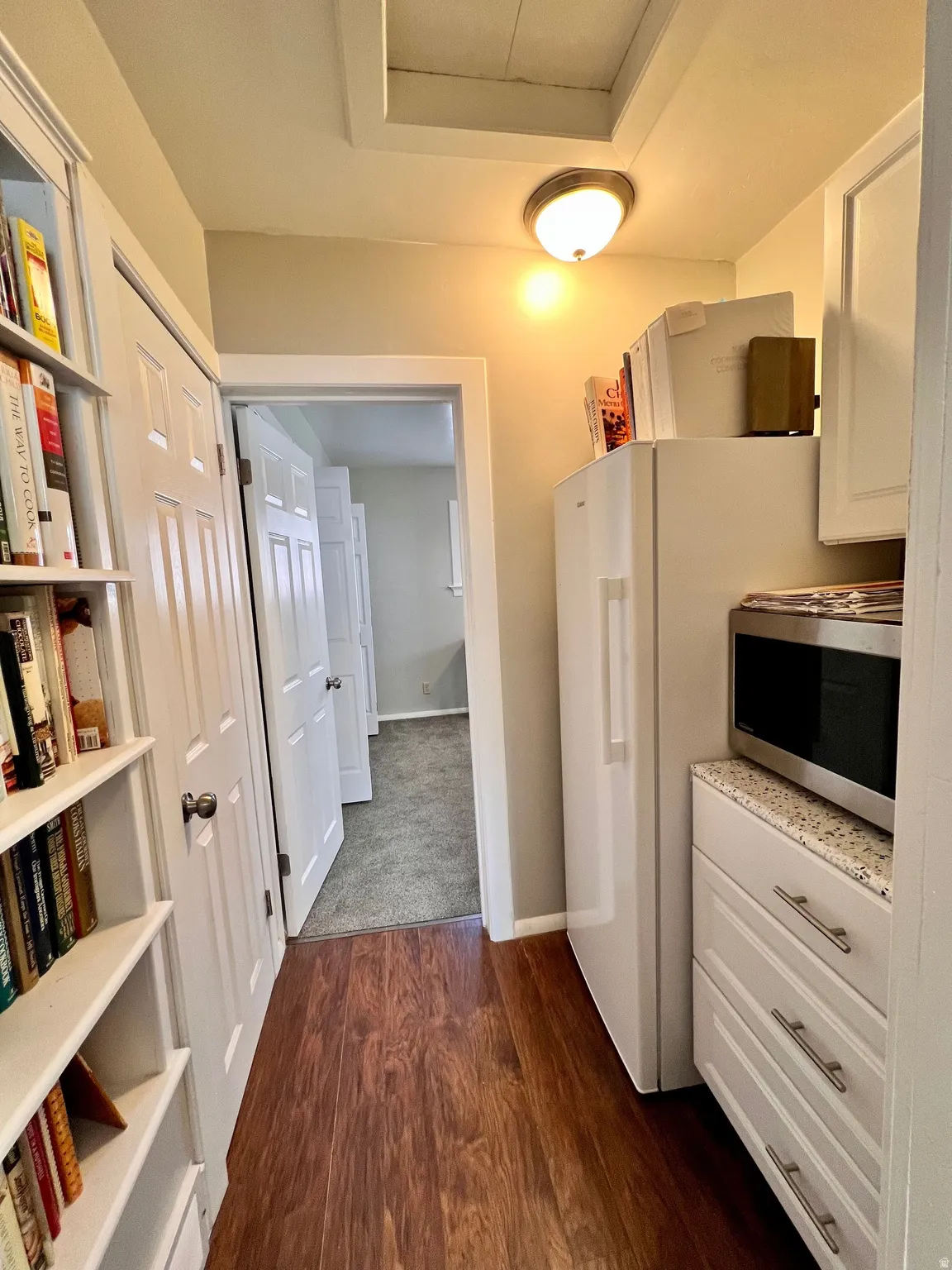 Kitchen featuring stainless steel microwave, white cabinets, dark wood-type flooring, and freestanding refrigerator
