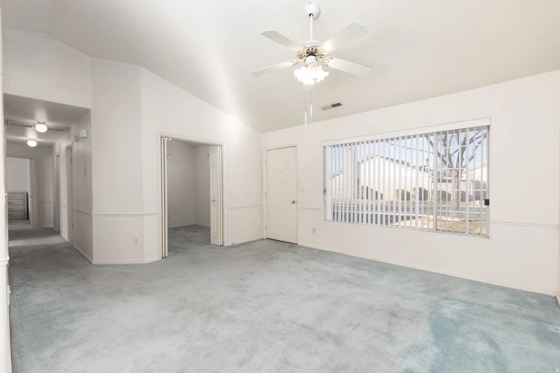 Unfurnished living room featuring a ceiling fan, vaulted ceiling, and light colored carpet