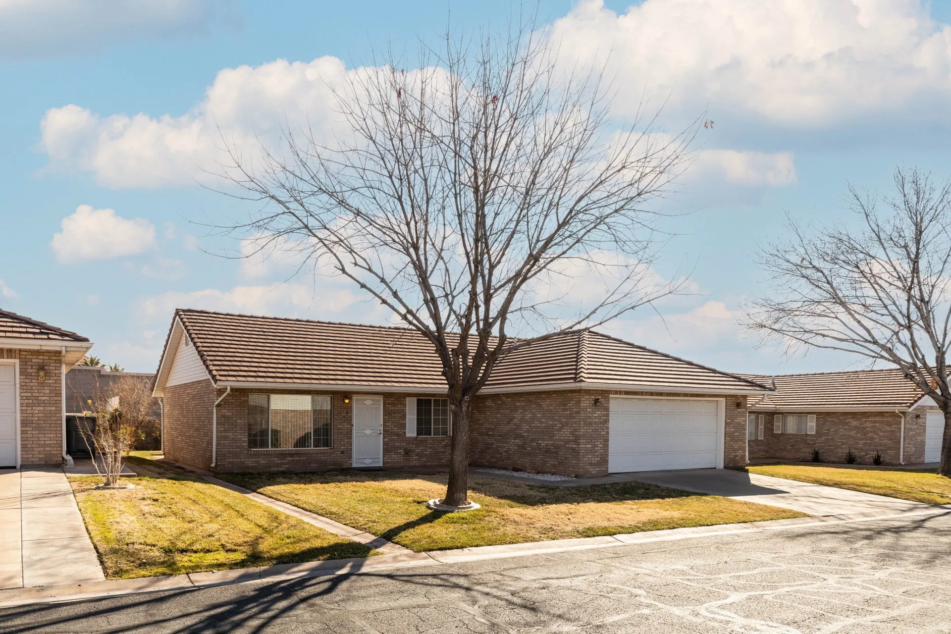 Ranch-style house featuring a tiled roof, a front lawn, concrete driveway, and brick siding