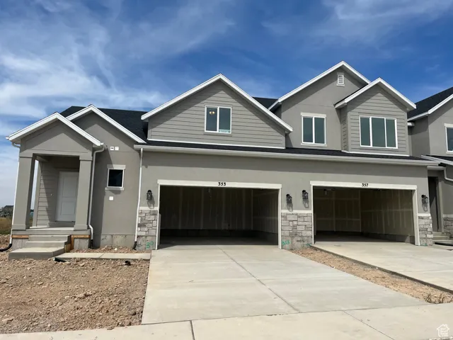 View of front of property with stone siding, stucco siding, driveway, and a garage