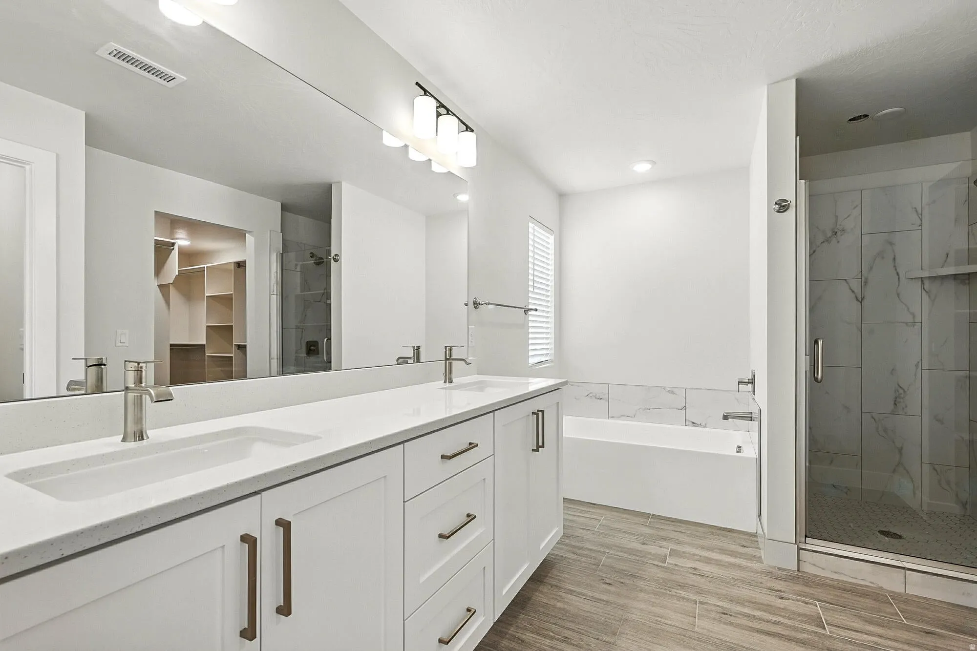 Full bath with a marble finish shower, double vanity, a spacious closet, wood tiled floors, and a garden tub