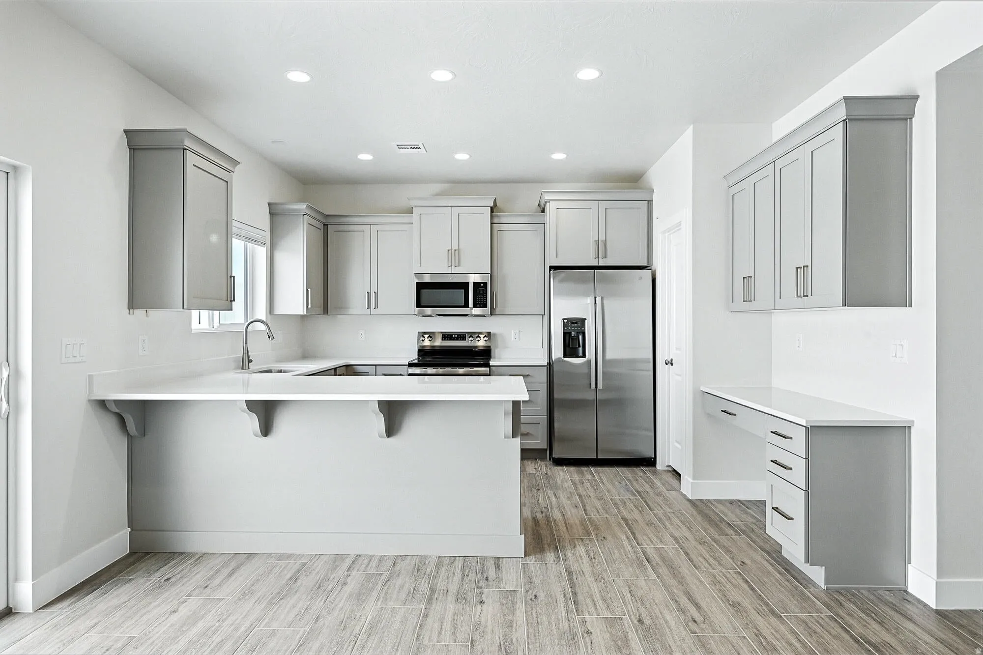 Kitchen featuring gray cabinets, a kitchen breakfast bar, stainless steel appliances, a peninsula, and wood tiled floors