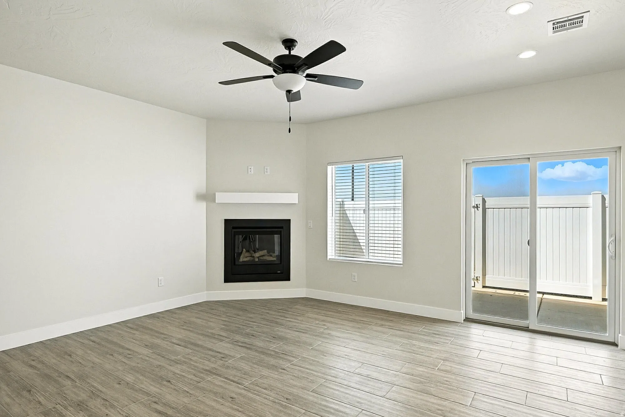 Unfurnished living room featuring light wood finished floors, a glass covered fireplace, ceiling fan, and recessed lighting