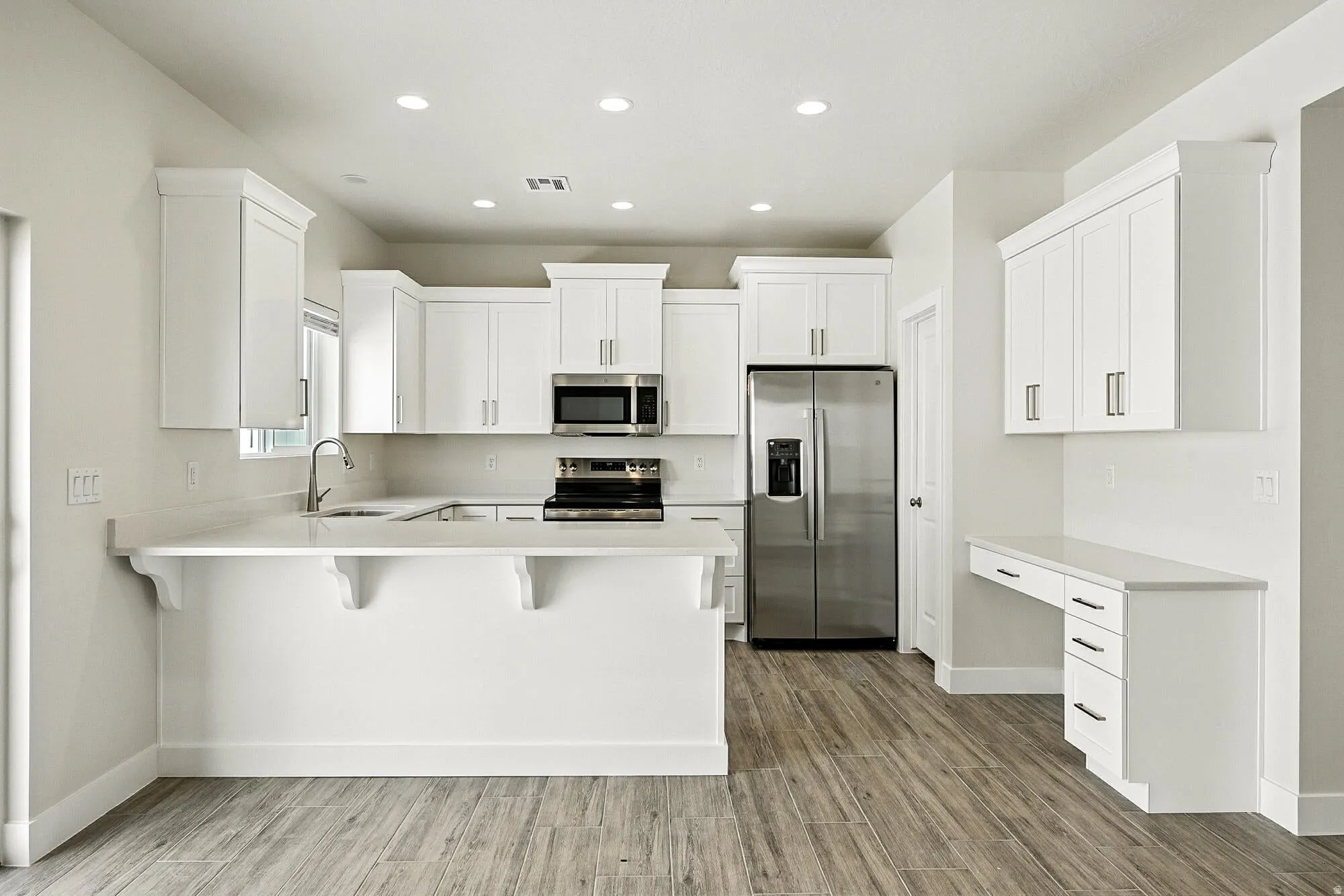 Kitchen featuring a breakfast bar area, stainless steel appliances, white cabinetry, a peninsula, and light wood-style flooring