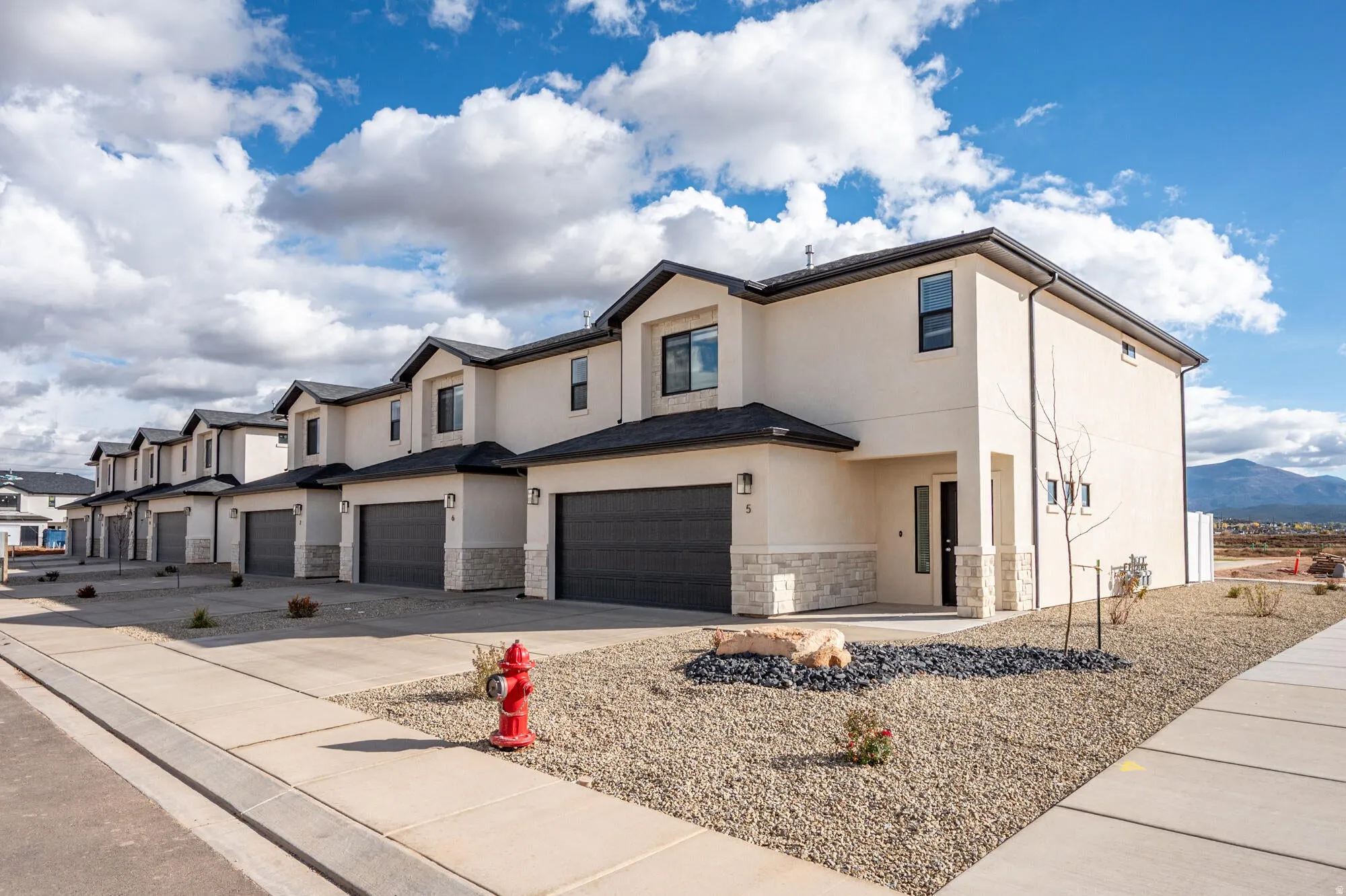 View of front of home featuring a garage, stucco siding, stone siding, and driveway